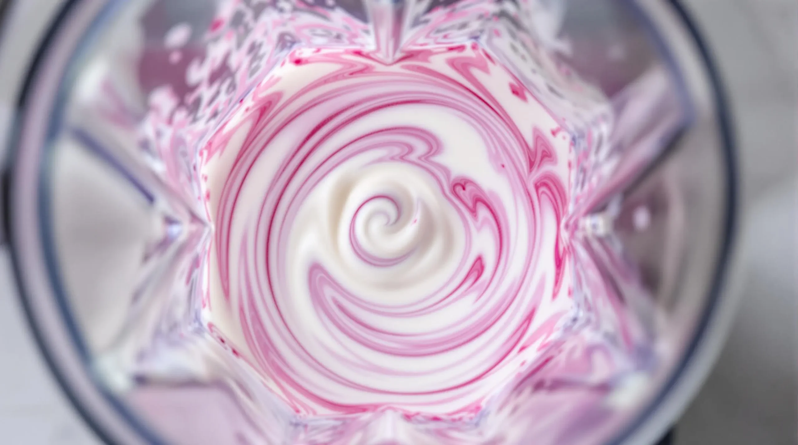 Vibrant pink berry puree swirling with coconut milk in blender, creating dynamic patterns during mid-blend action