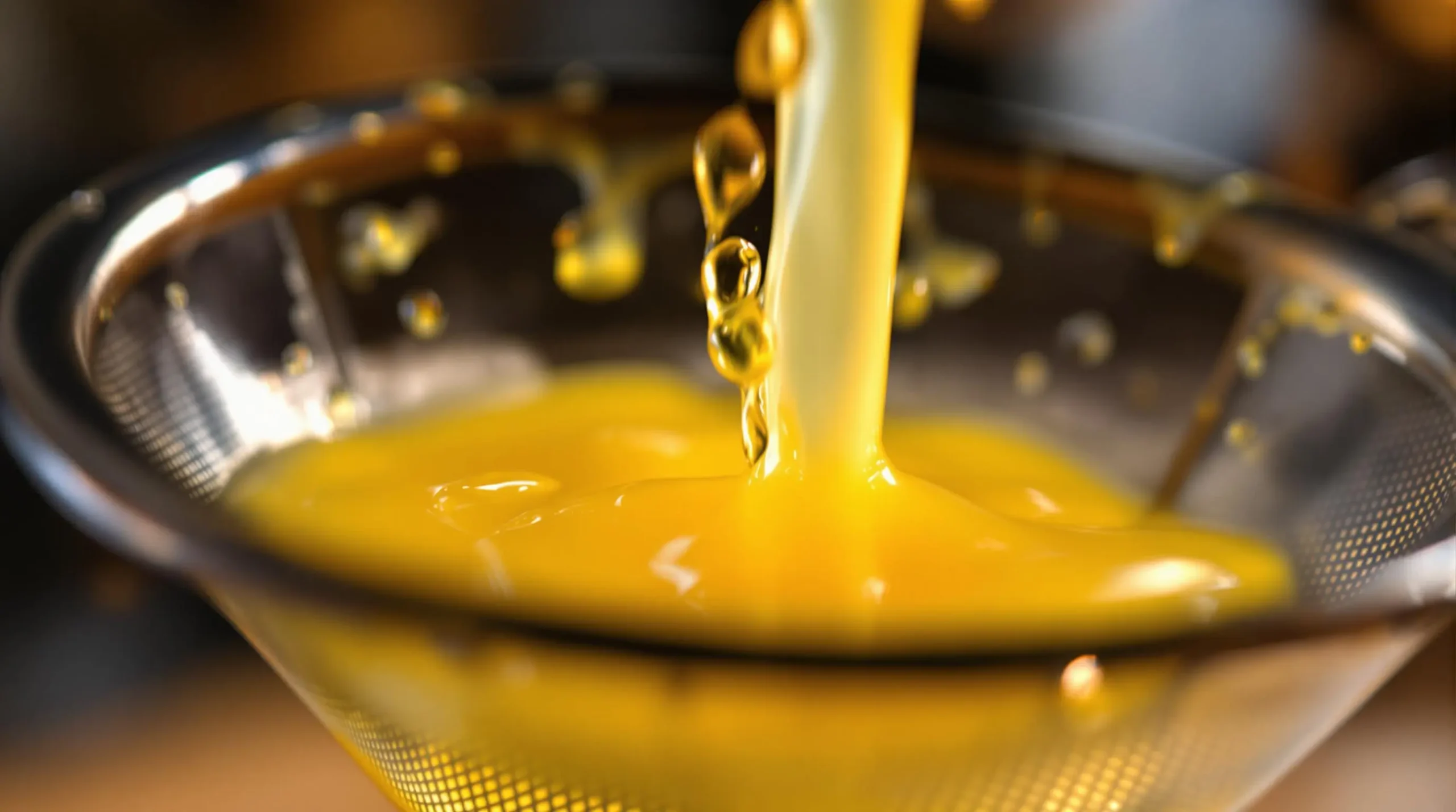 Golden pineapple juice streaming through fine-mesh strainer into martini glass, highlighting silky texture and liquid motion