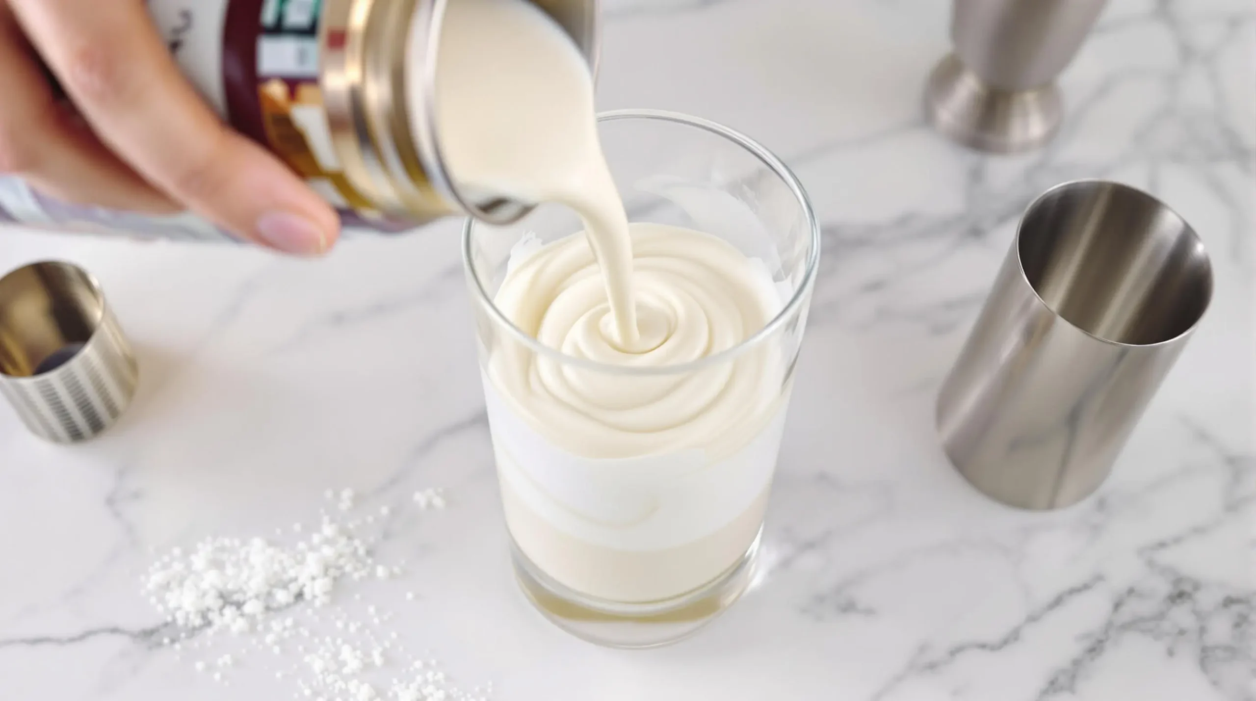 Layering RumChata and coconut cream in glass shaker showing distinct cream swirls against marble countertop